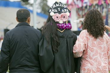 graduating student with parents, "gracias ama y apa" thank you mother and father